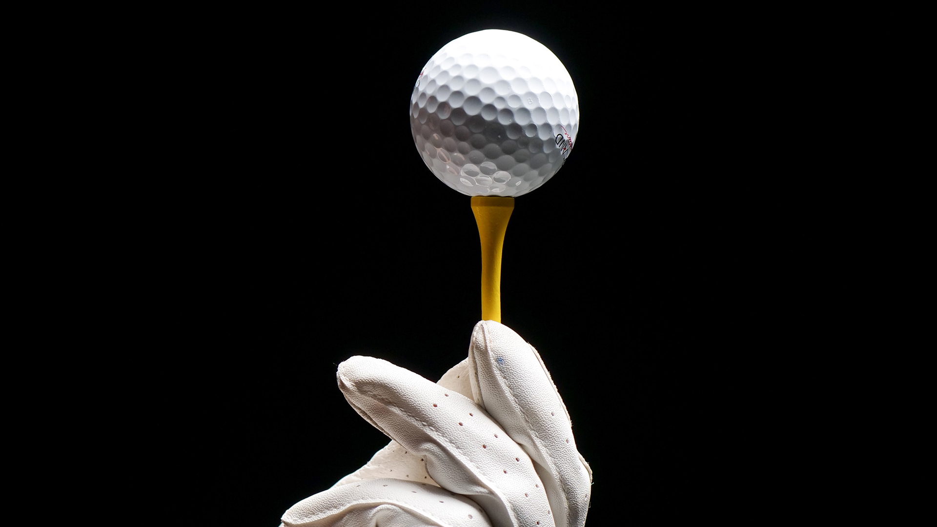 Una foto estilo artístico de una bola de golf sujeta por unos guantes de piel blanca