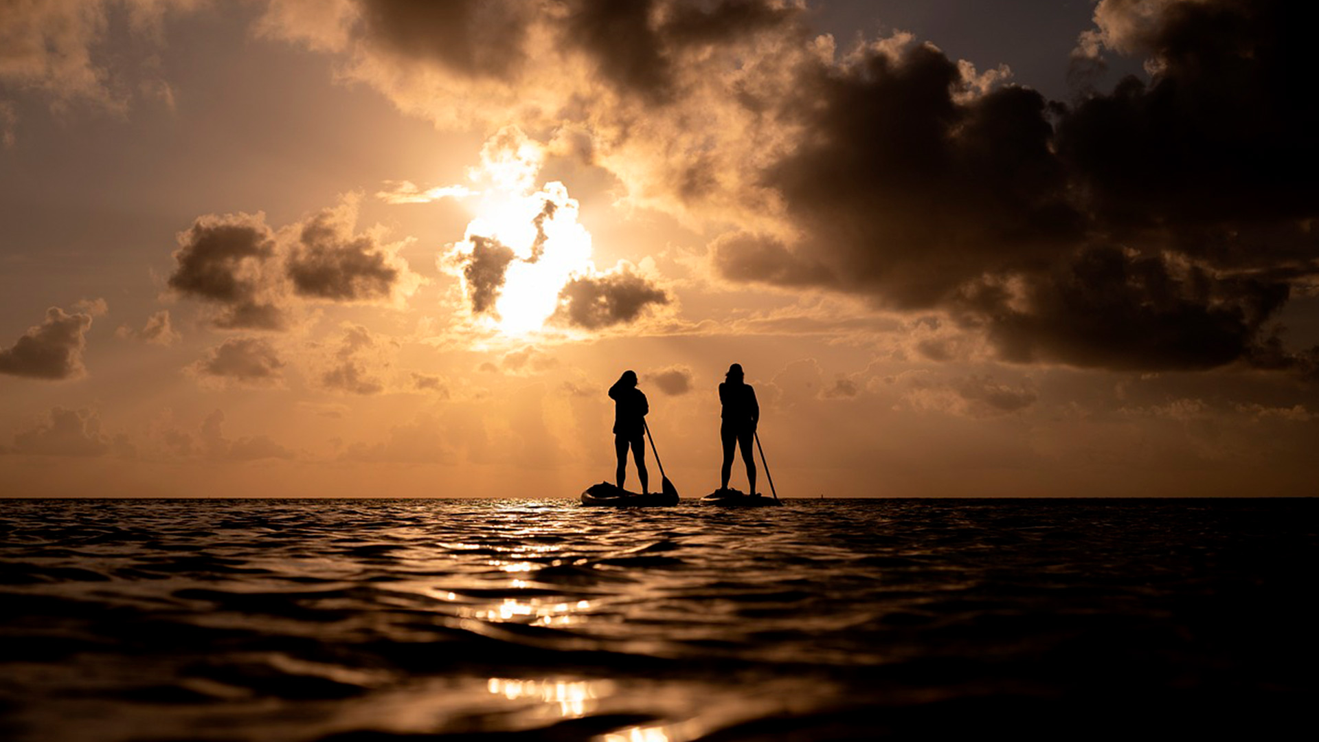 Dos siluetas personas practicando Paddle surf en Almería al atardecer